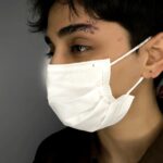 Person wearing a white face mask with two silver eyebrow piercings.