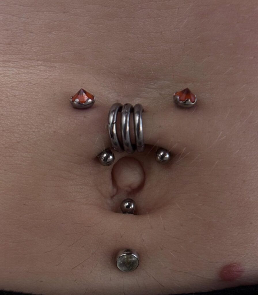 Navel piercings featuring a central triple ring barbell and orange gemstone studs.