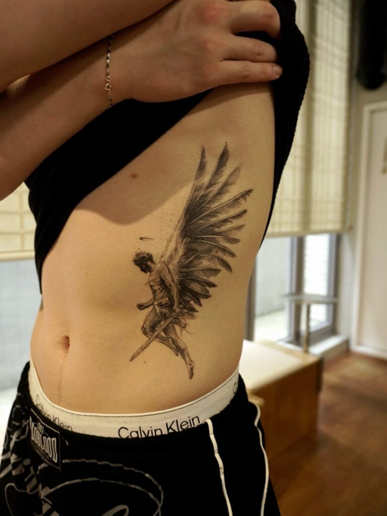 Angel tattoo with large wings on a person's side ribcage area.