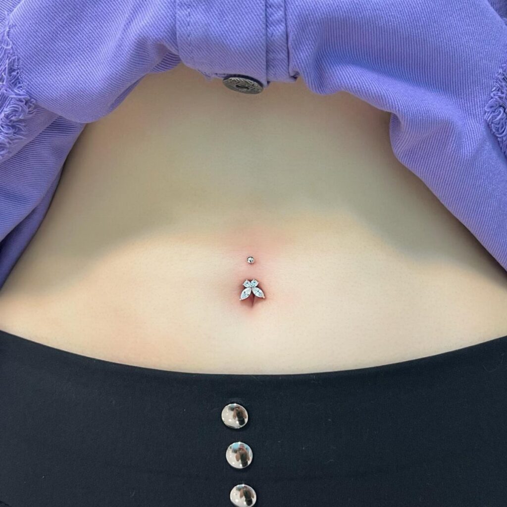 Belly button piercing with a silver butterfly jewel on a person's midriff.