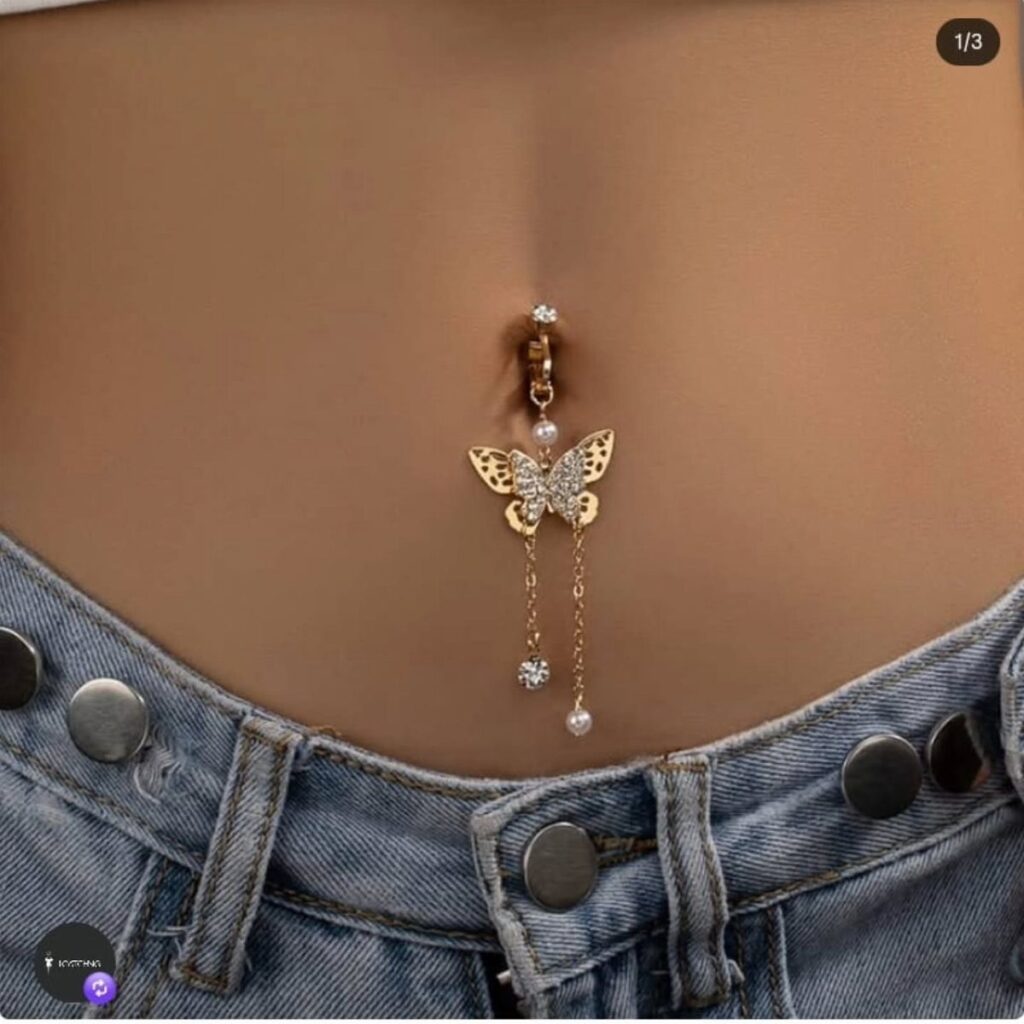 Gold-tone belly piercing with a crystal butterfly charm and dangling pearl chains.
