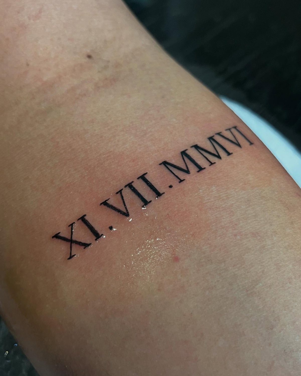 Roman numeral date tattoo XI.VII.MMVI inked in black on a person's skin