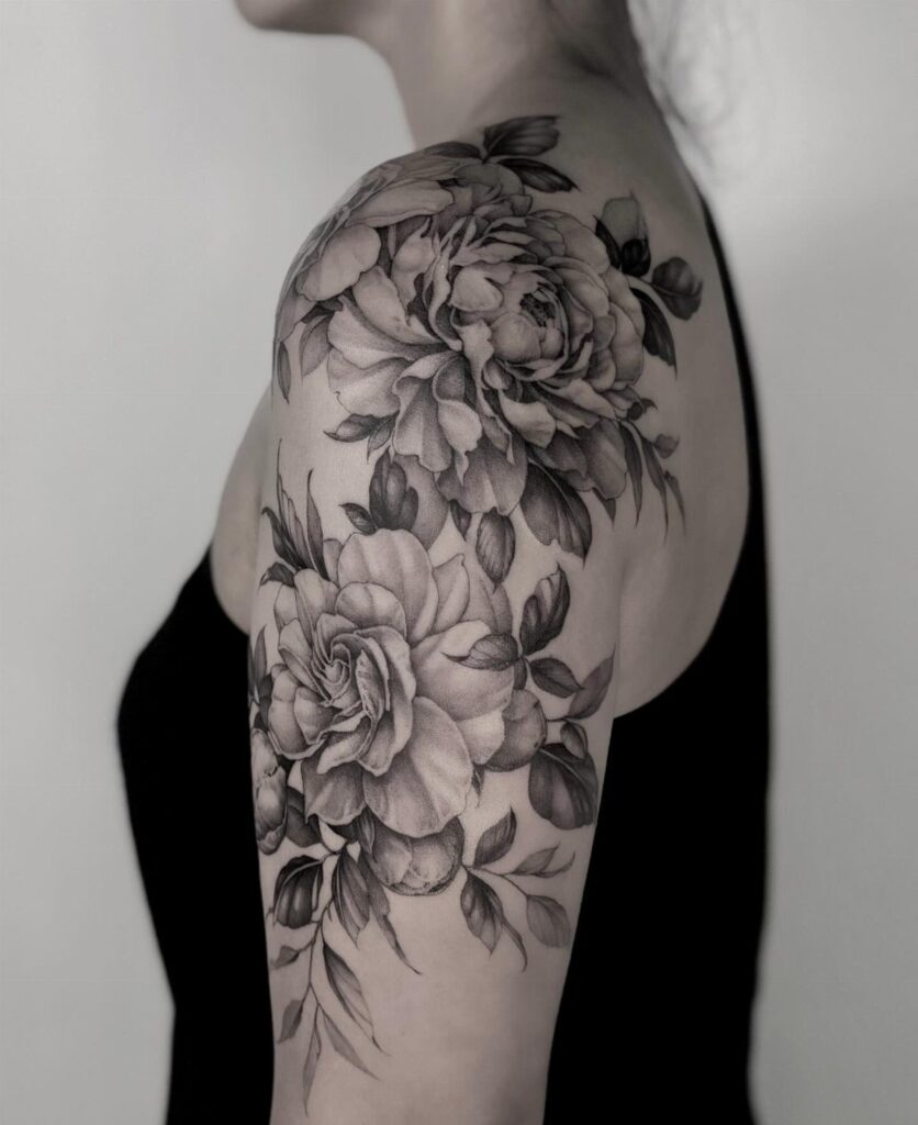 Black and grey floral tattoo of peonies on a person's upper arm and shoulder