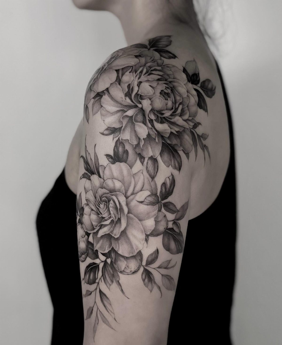 Black and grey floral tattoo of peonies on a person's upper arm and shoulder