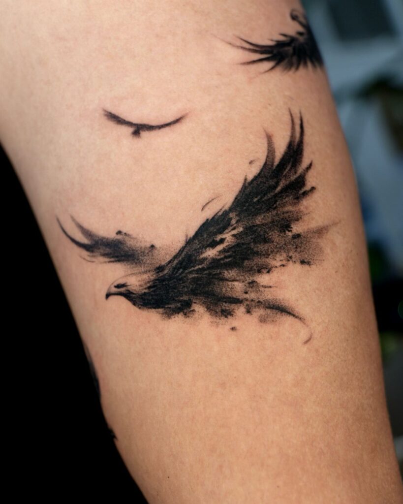 Black bird tattoo in flight with artistic ink splatters on human skin.