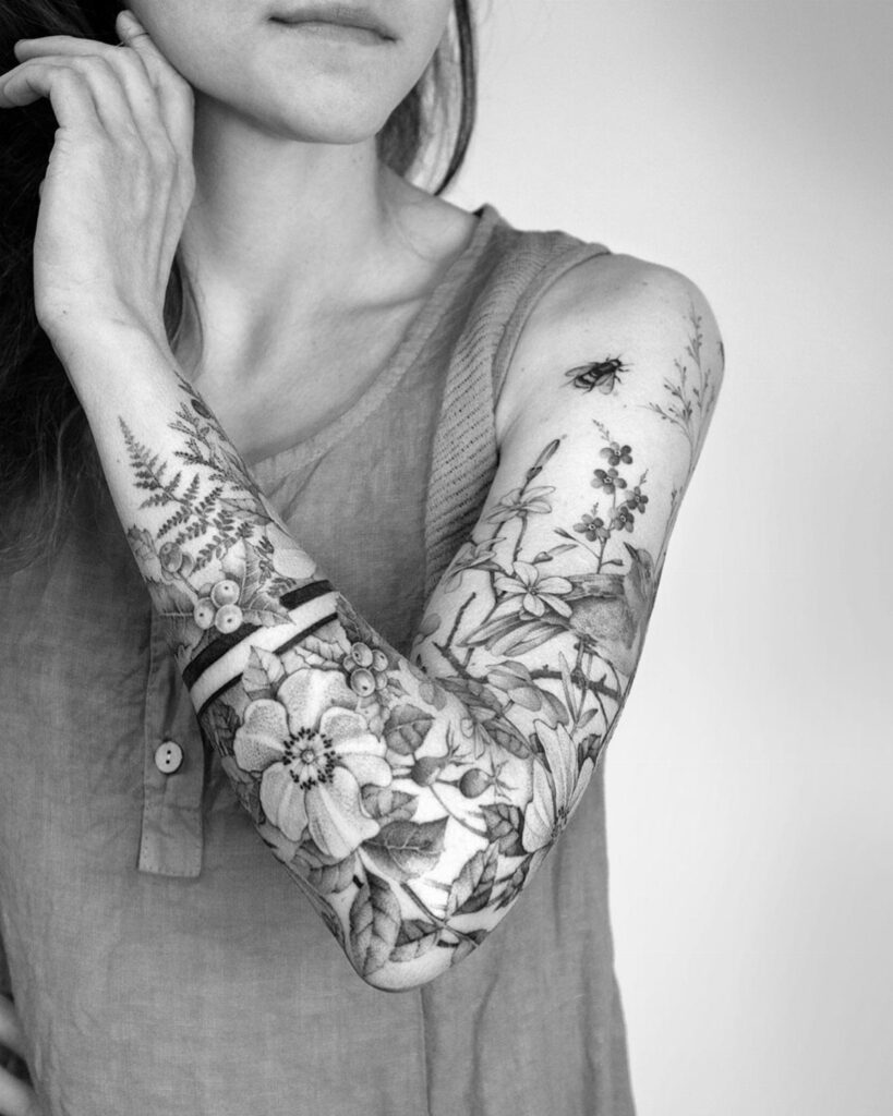 Botanical tattoo sleeve with flowers and ferns on a person's arm.