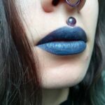 Person with blue lipstick and a purple bead Medusa piercing above the lip.