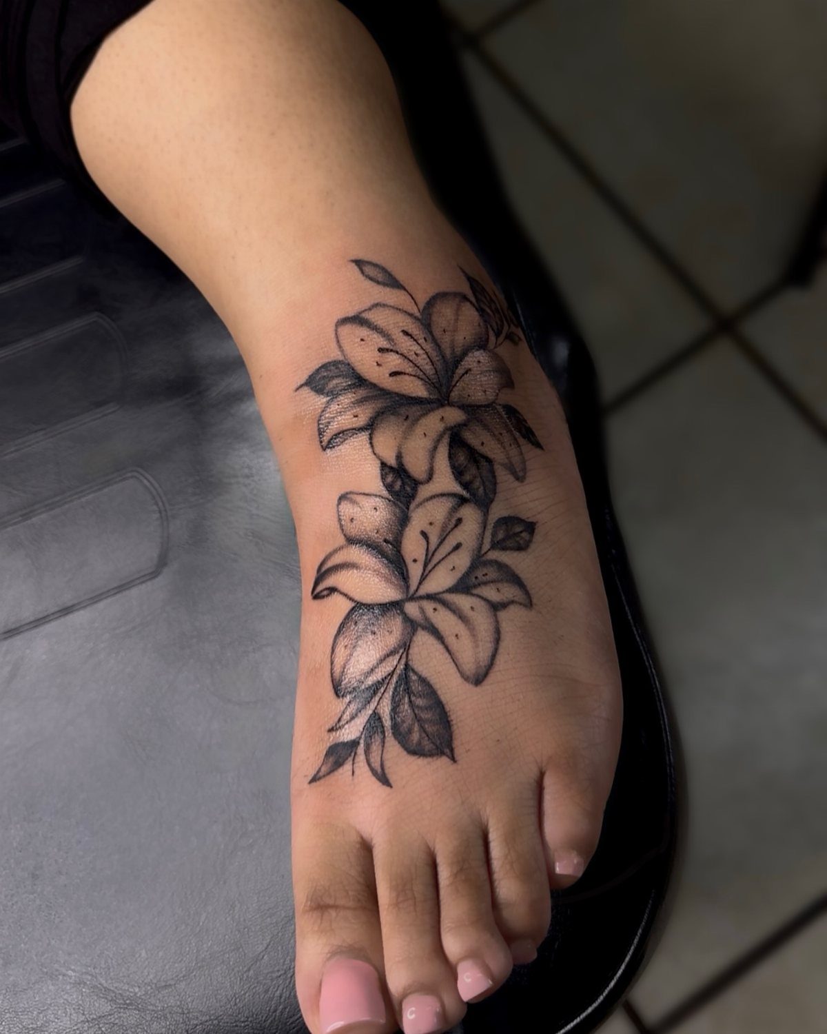 Lily flower tattoo on the top of a person's foot with pink toenails.