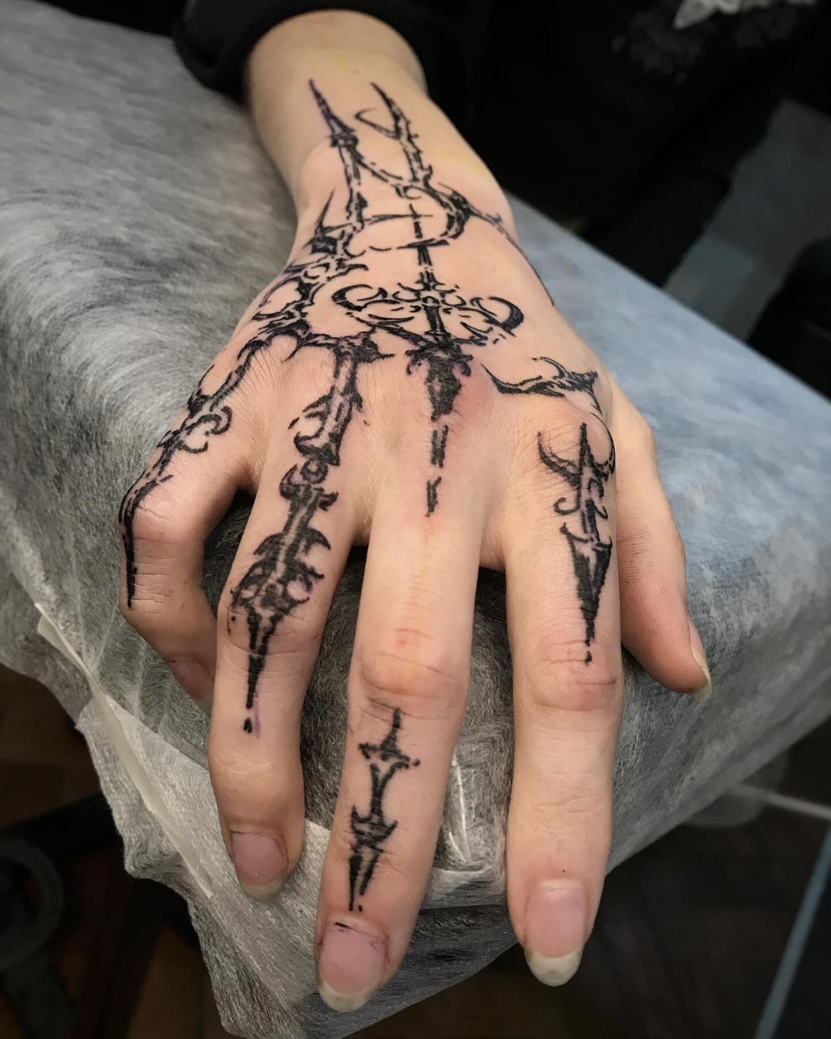 Hand with a black cybersigilism tattoo featuring sharp, intricate, futuristic linear patterns.