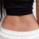 Two silver dermal piercings located in the dimples of a person's lower back.