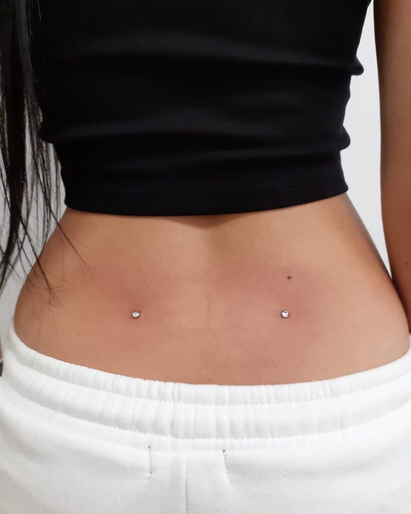 Two silver dermal piercings located in the dimples of a person's lower back.