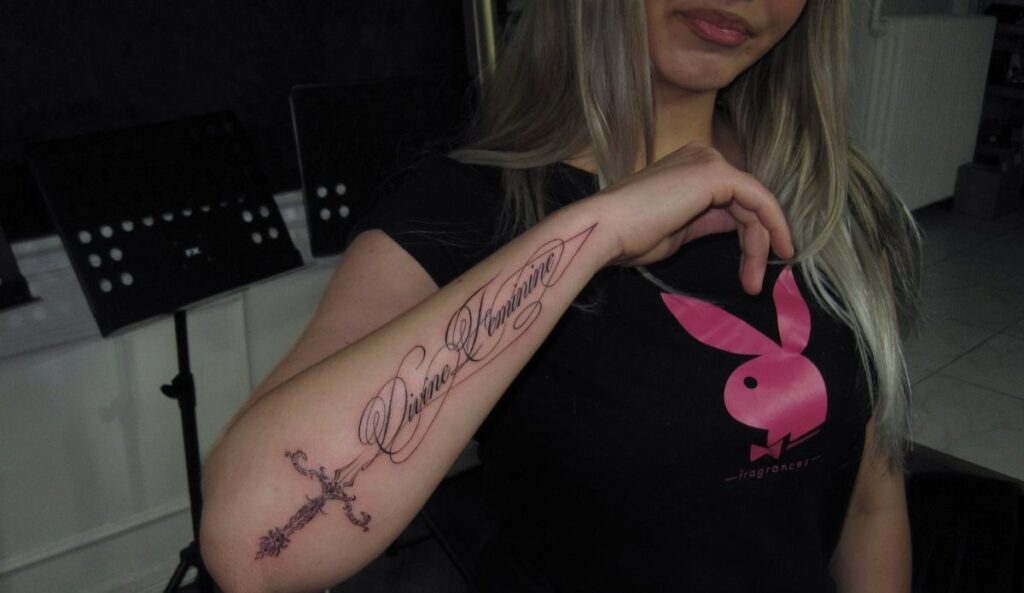 Forearm tattoo with the words Divine Feminine in elegant black cursive script.
