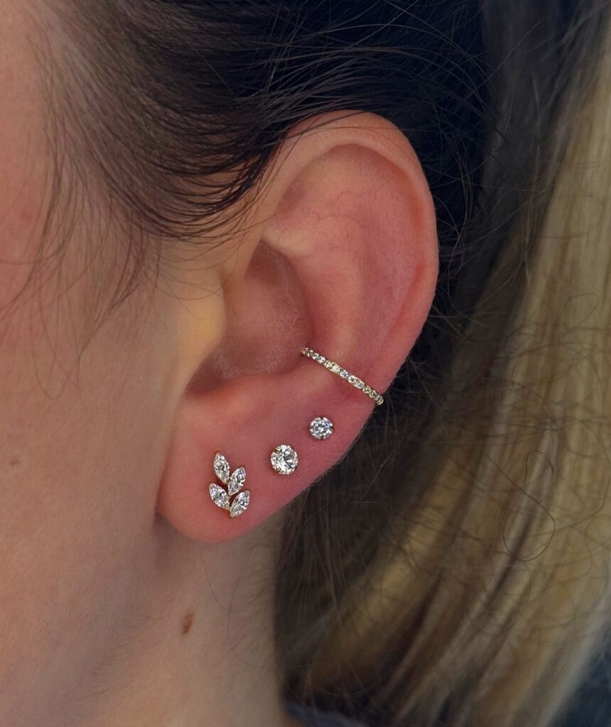 Ear with a crystal conch piercing and a trio of sparkling lobe studs.
