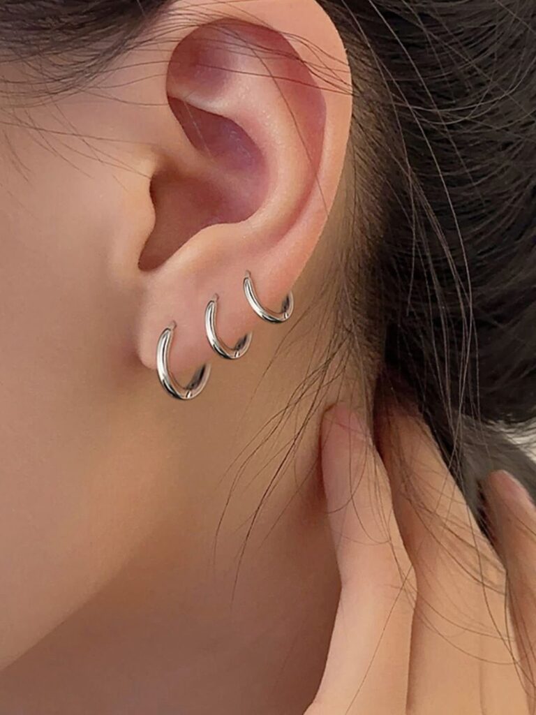 Three small silver hoop earrings in a row of earlobe piercings.