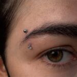 Person's eyebrow and eye featuring a silver ball and gemstone piercing.
