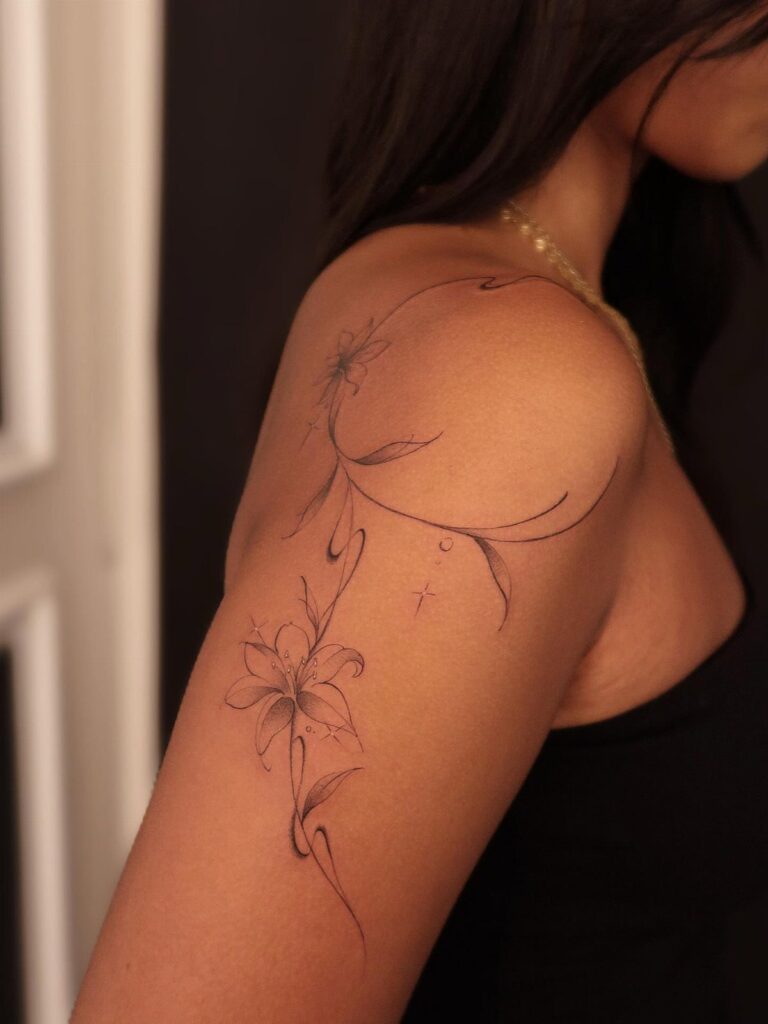 Fine-line lily flower tattoo on a woman's shoulder and upper arm.