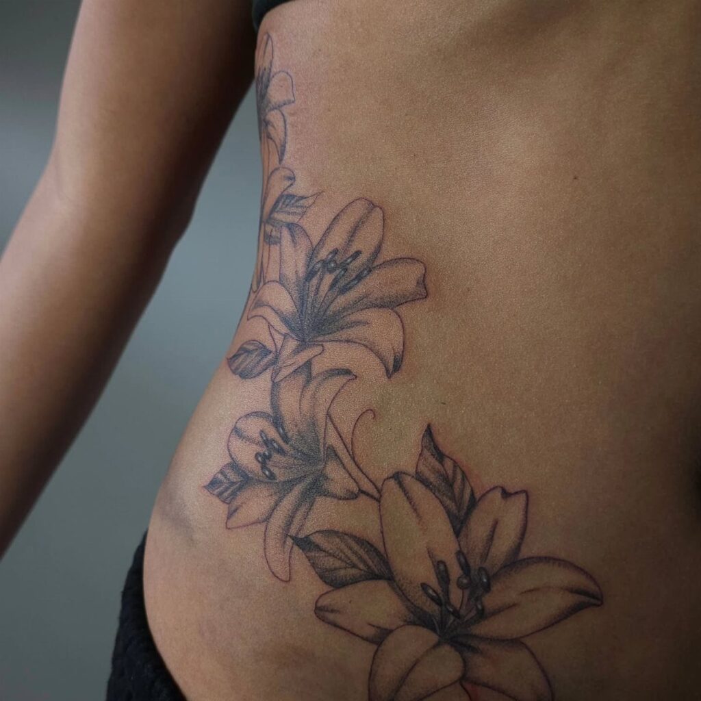 Lily flower tattoo in black and grey ink on a woman's ribcage.