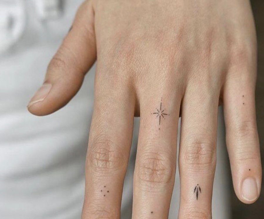 Hand and fingers with small black ink tattoos of a star and dots
