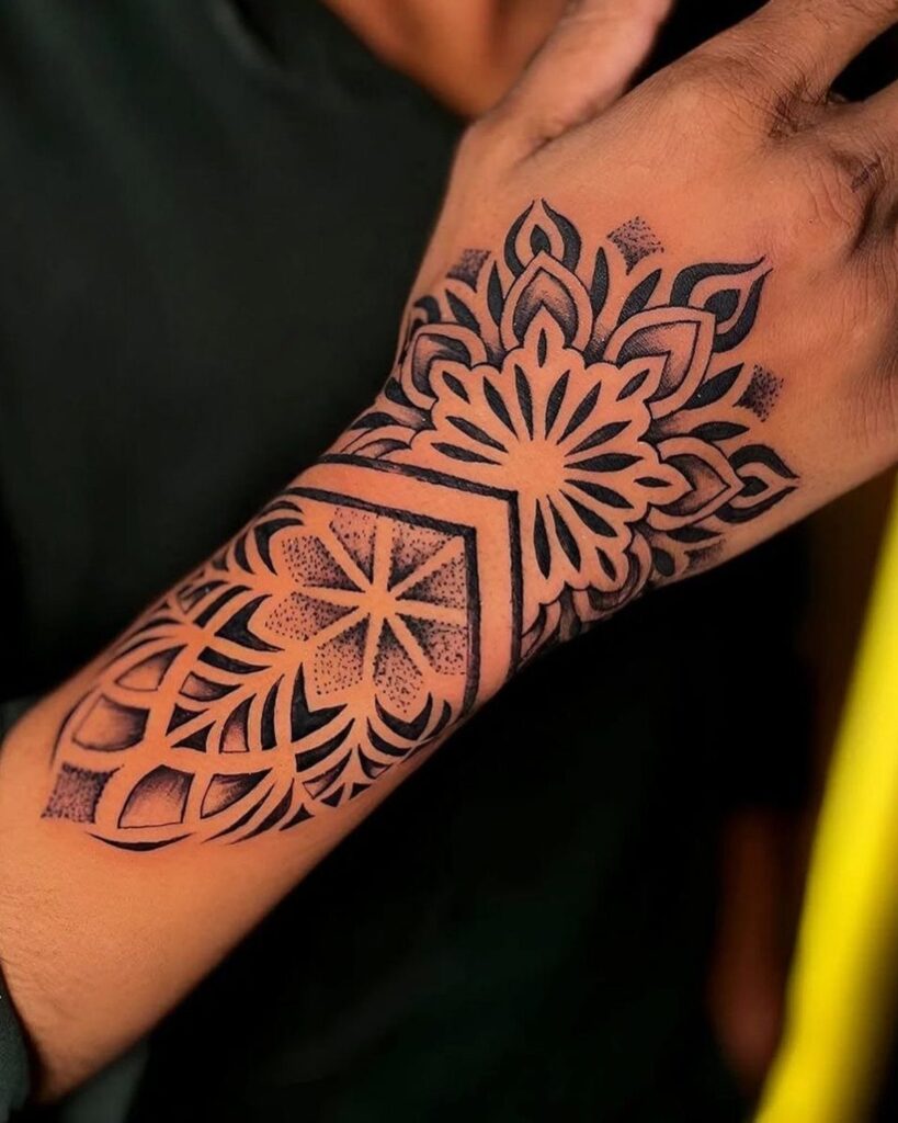 Symmetrical mandala tattoo on the back of a hand and wrist in black ink.