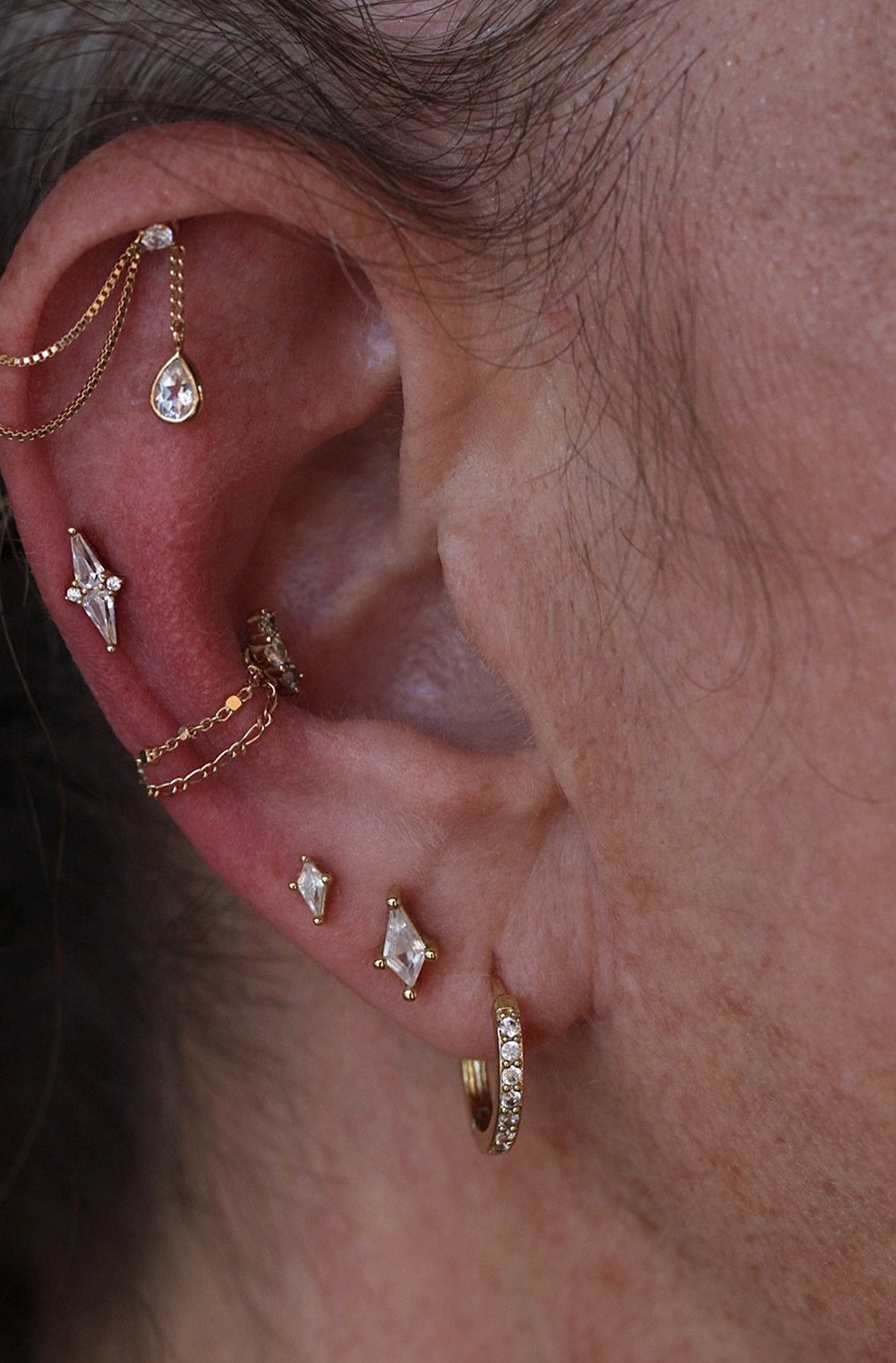 Ear with multiple gold piercings and a hanging chain with a teardrop gemstone.