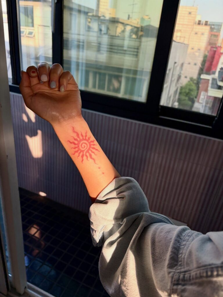 Henna tattoo of a stylized sun on a person's forearm near a window.