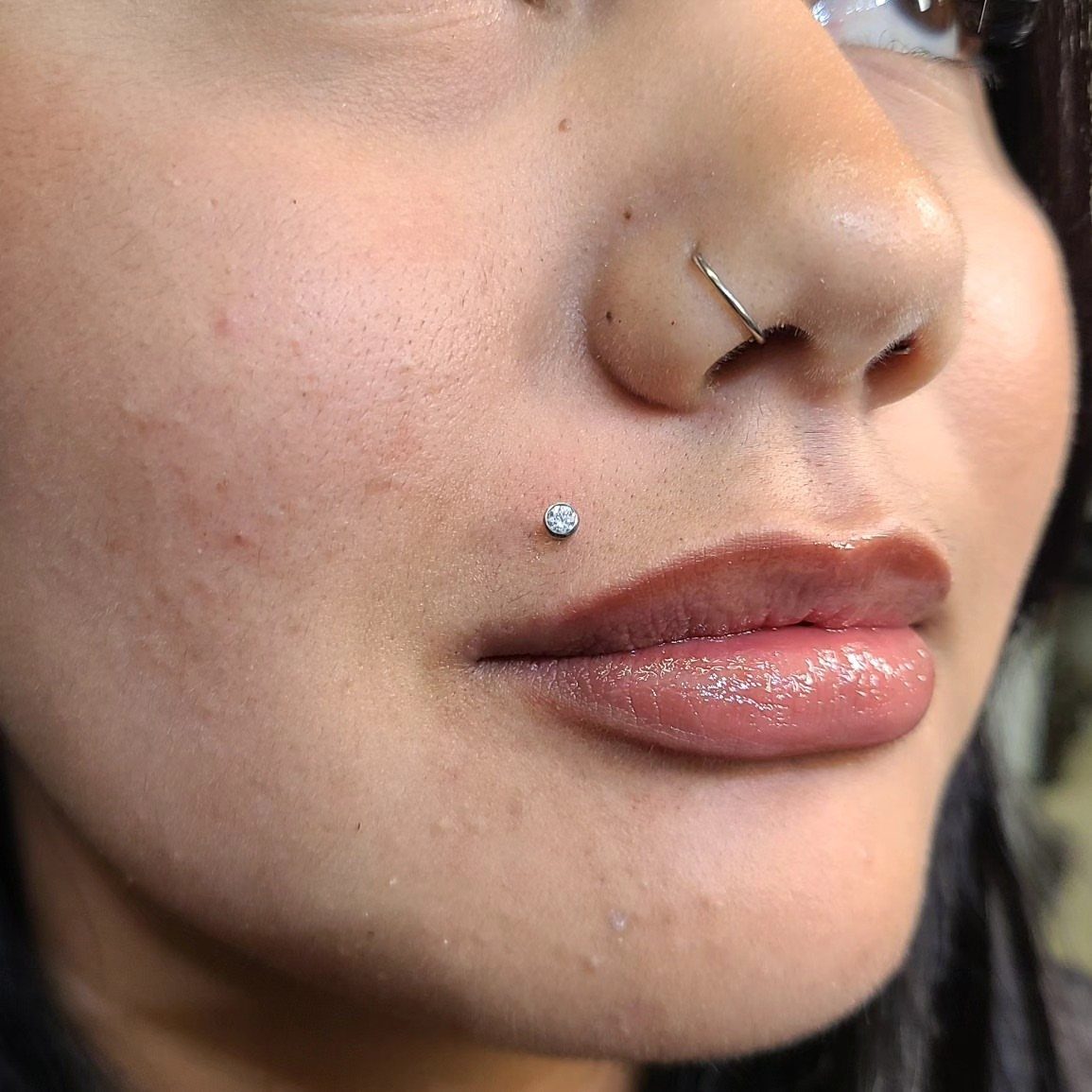 Person with a sparkling Monroe piercing on the upper lip and a nose hoop.
