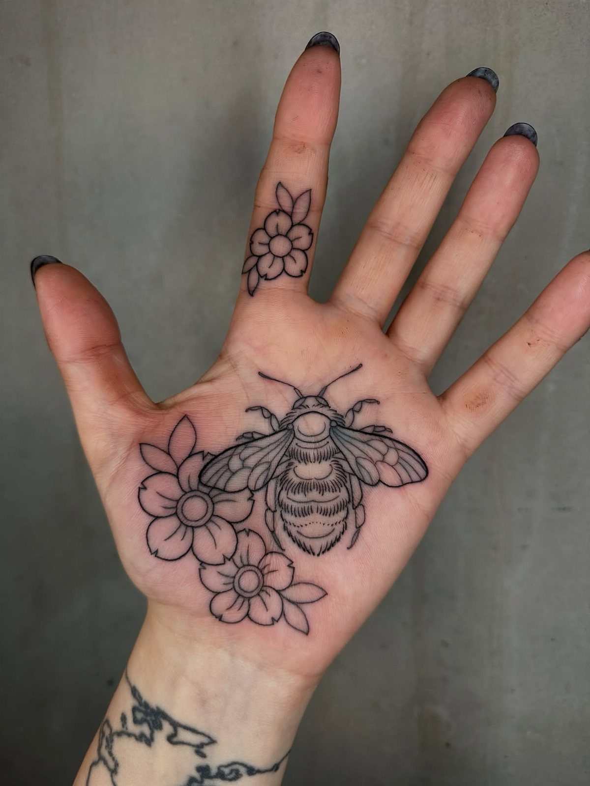 Bee and flower tattoos on an open human palm and ring finger.