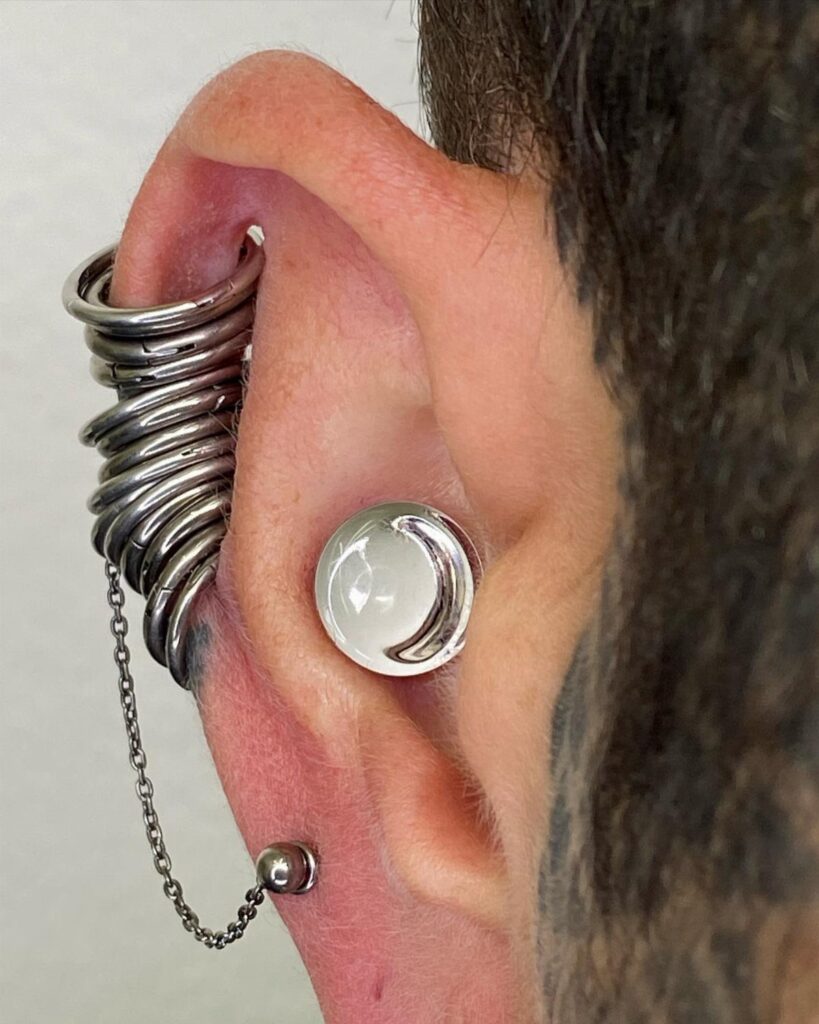 Human ear with a white moon conch piercing and stacked silver helix rings.