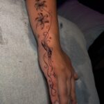 Black ink tattoo of lilies and swirls on a forearm and hand