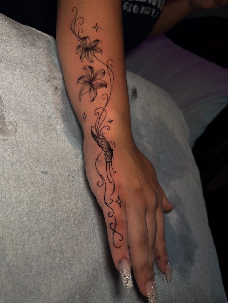 Black ink tattoo of lilies and swirls on a forearm and hand