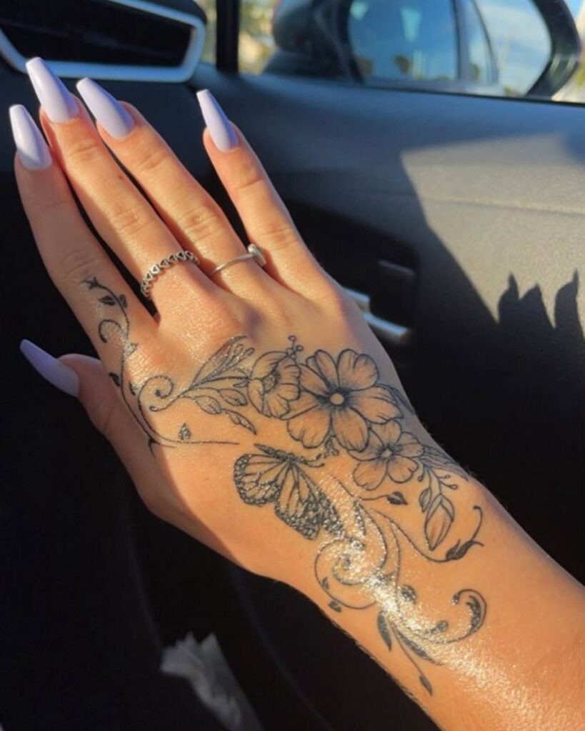 Hand with floral and butterfly tattoo and light purple long nails inside a car
