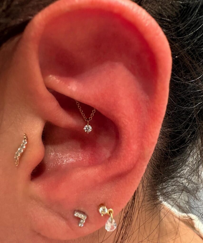 Human ear with a diamond rook piercing and gold lobe jewelry.