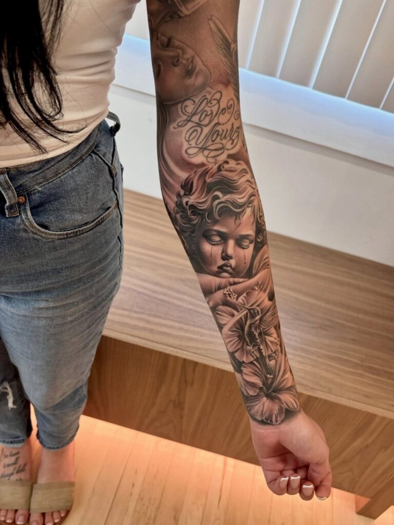 Realistic black and grey cherub tattoo on a person's forearm with cloud details.