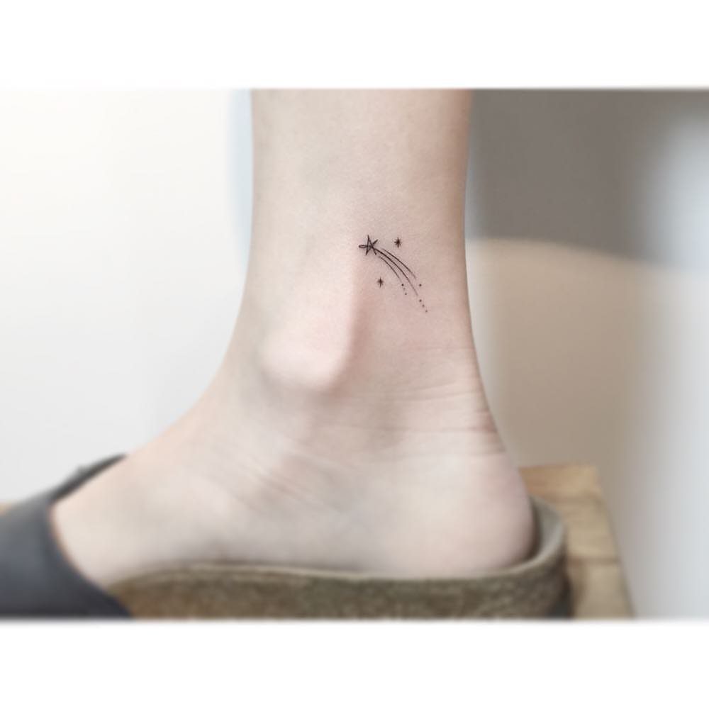 Small shooting star tattoo with a dotted trail on a person's ankle.