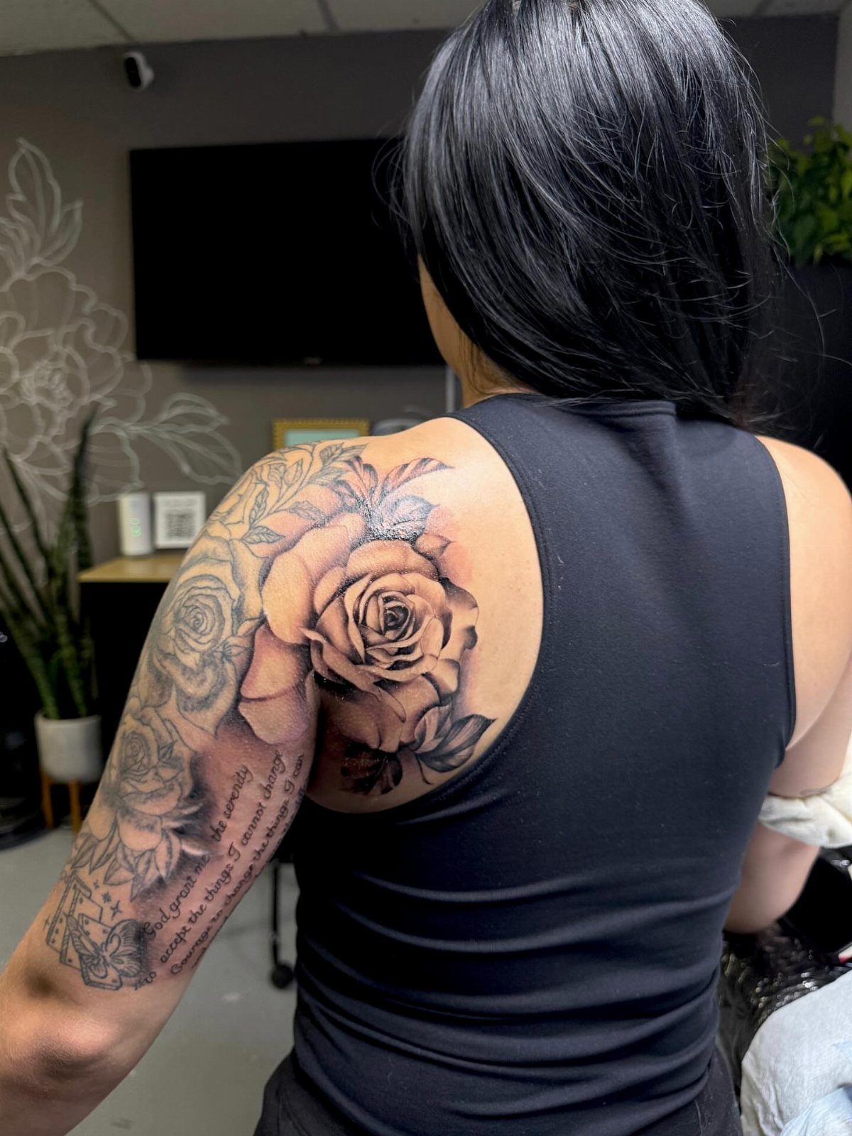 Large black and grey rose tattoo on the side arm and shoulder of a person.
