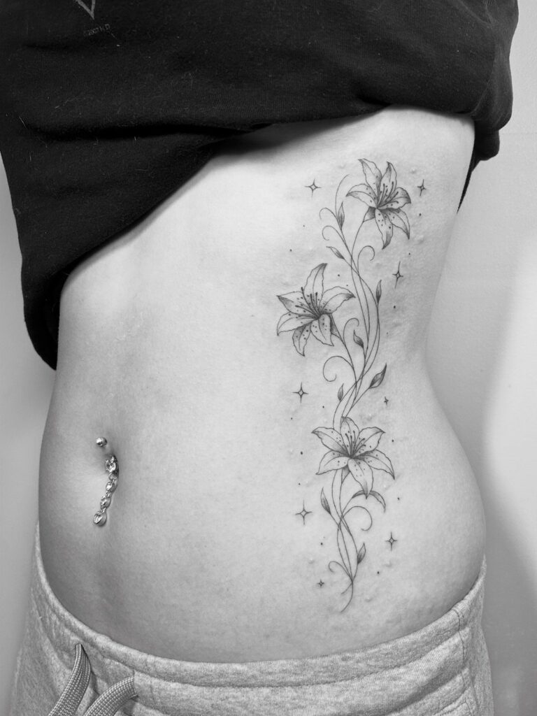 Floral lily tattoo with vines and stars on a person's side stomach.