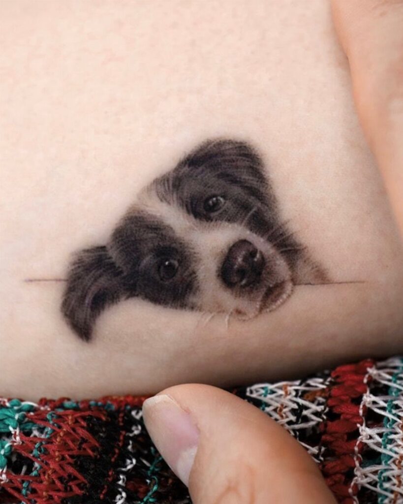 Realistic dog portrait tattoo on skin showing a grey and white puppy head.
