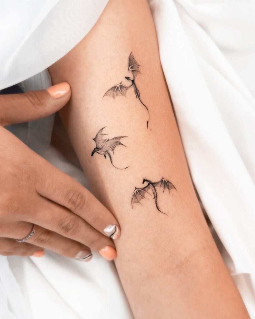Three small black ink dragon tattoos on a person's forearm