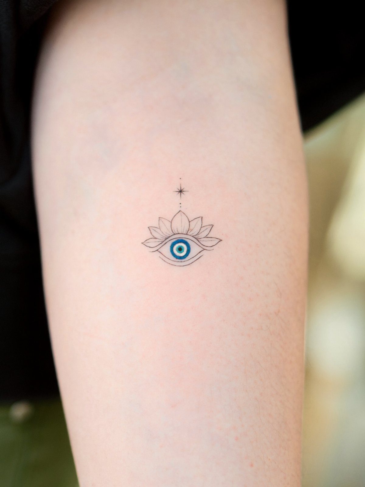 Small eye tattoo with a blue iris inside a lotus flower on an arm