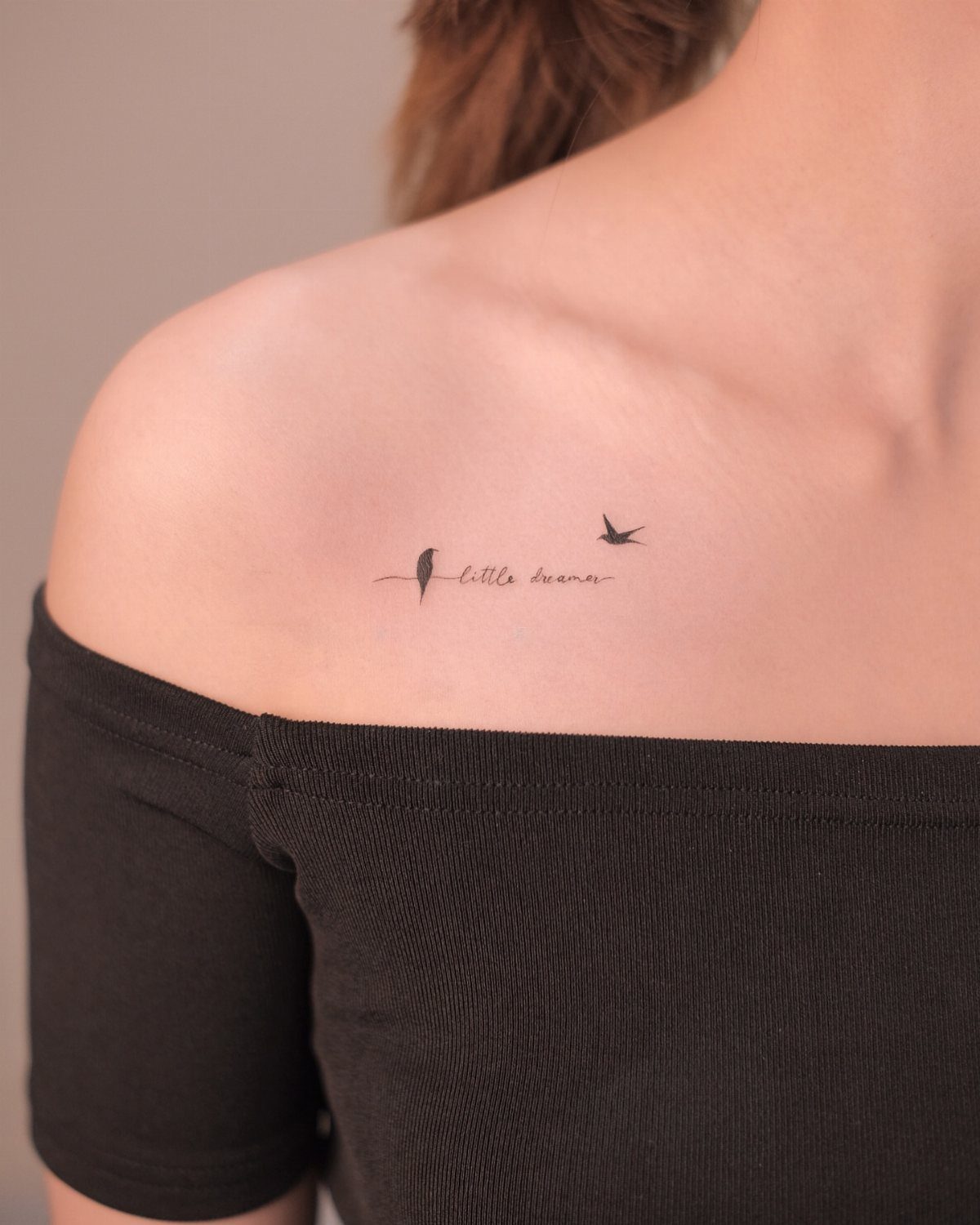 Small black ink tattoo of a bird and text on a person's shoulder.