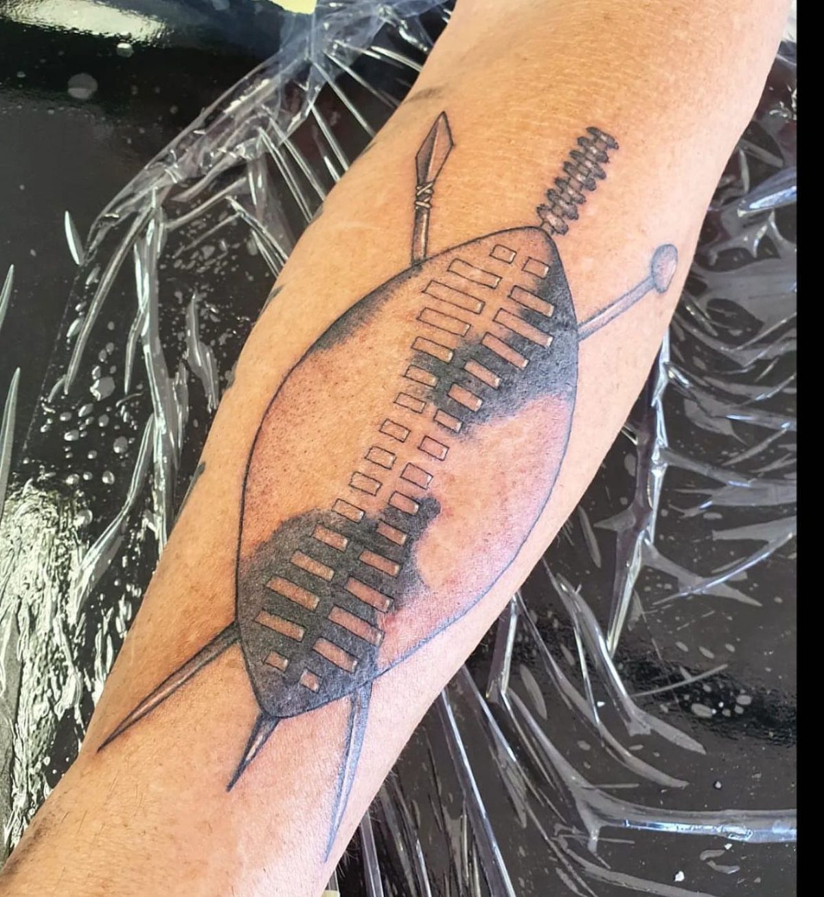 Zulu shield and spear tattoo on a person's forearm over plastic wrap