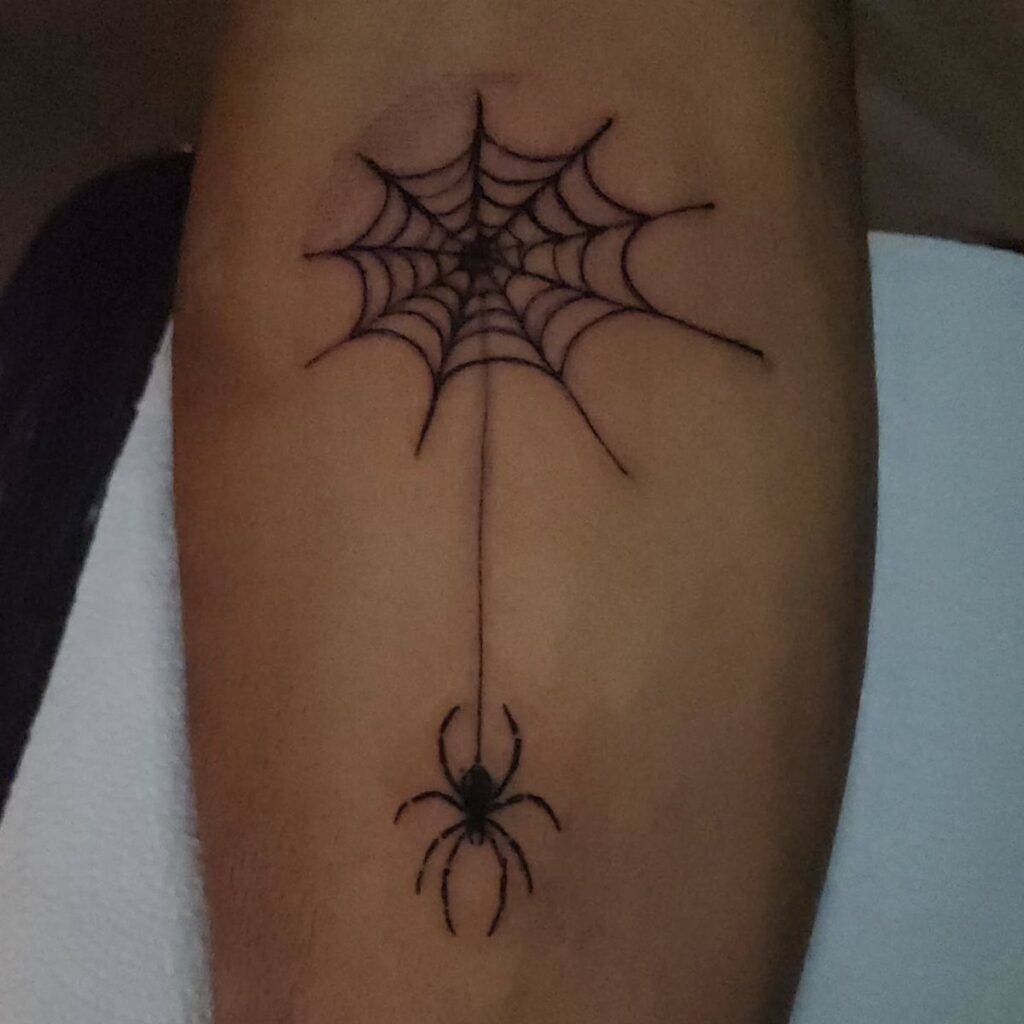 Black ink tattoo of a spider hanging from a web on skin