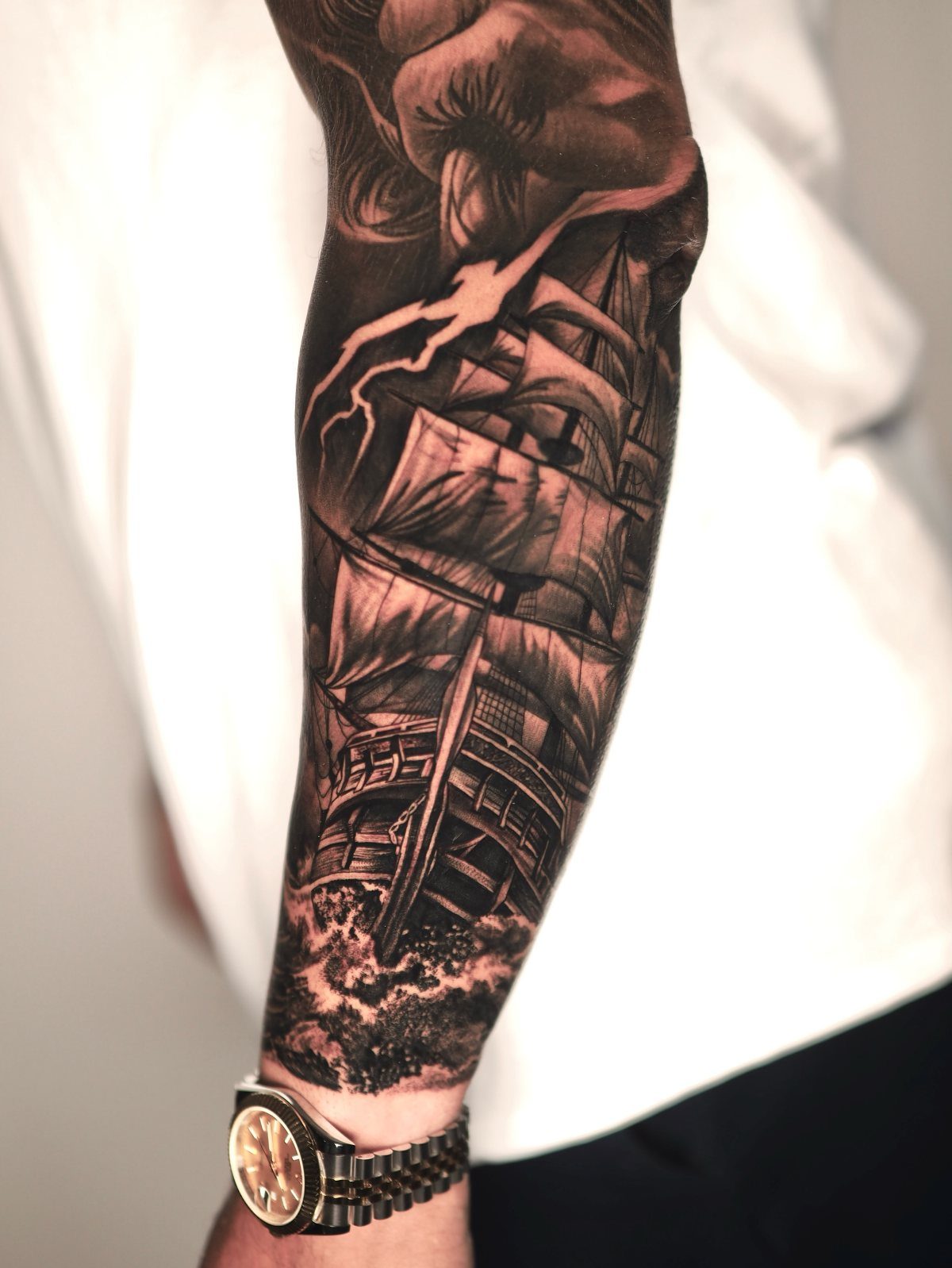 Detailed black and grey tattoo of a sailing ship on a person's forearm.