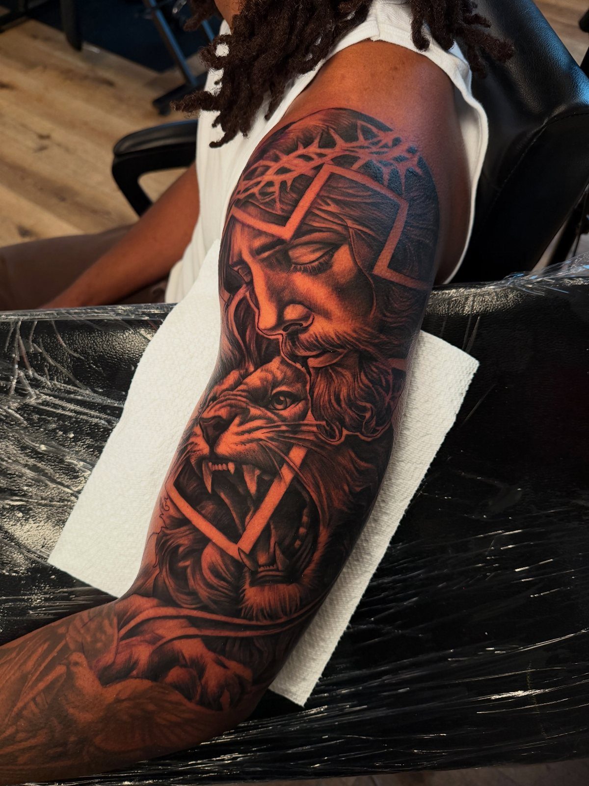 Detailed black ink tattoo of Jesus and a lion on dark skin arm