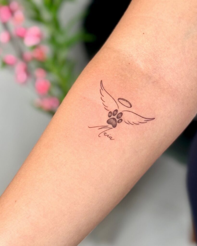 Dog paw print tattoo with angel wings and halo on a forearm