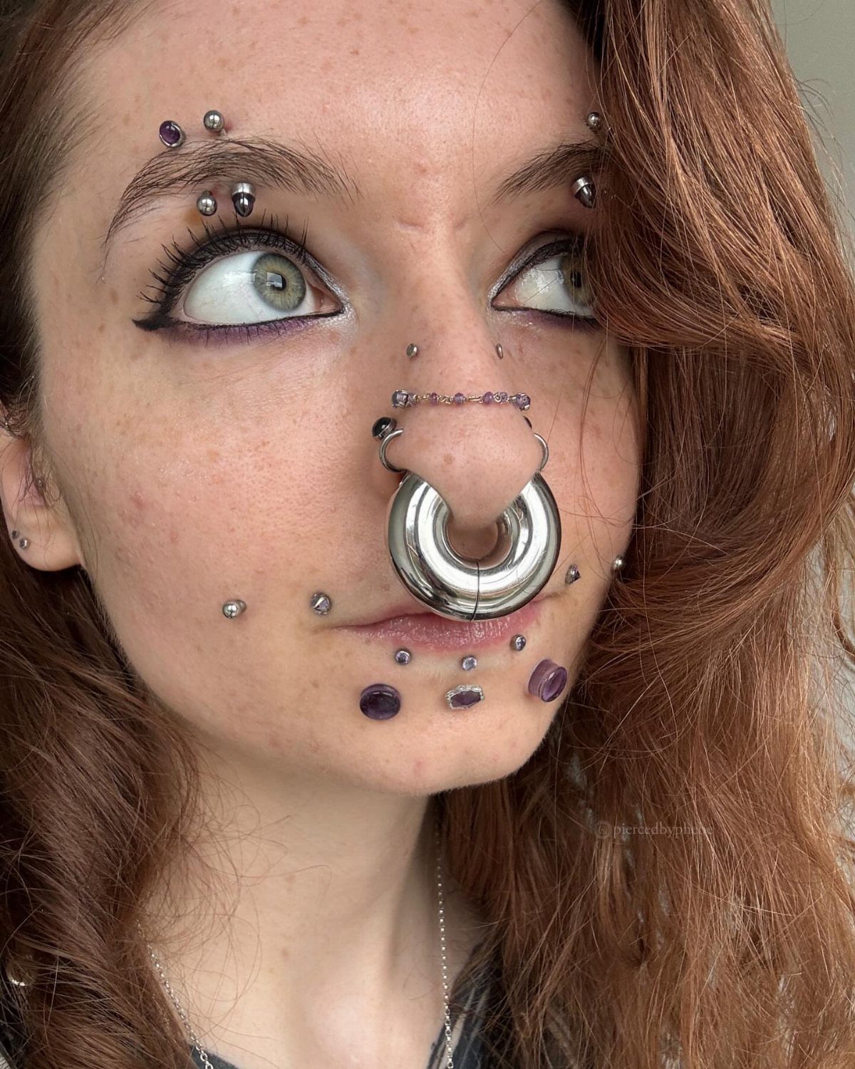 Person with red hair wearing a thick silver septum gauge and facial piercings.
