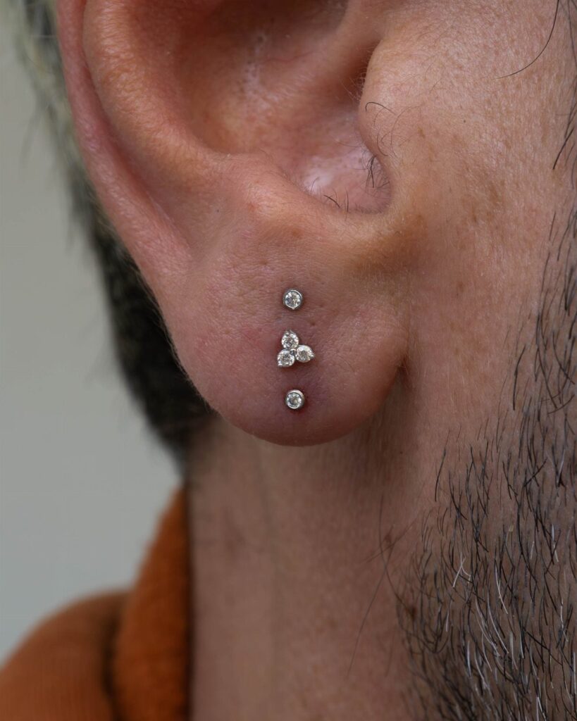 Ear lobe with three vertical piercings featuring clear diamond-like studs.
