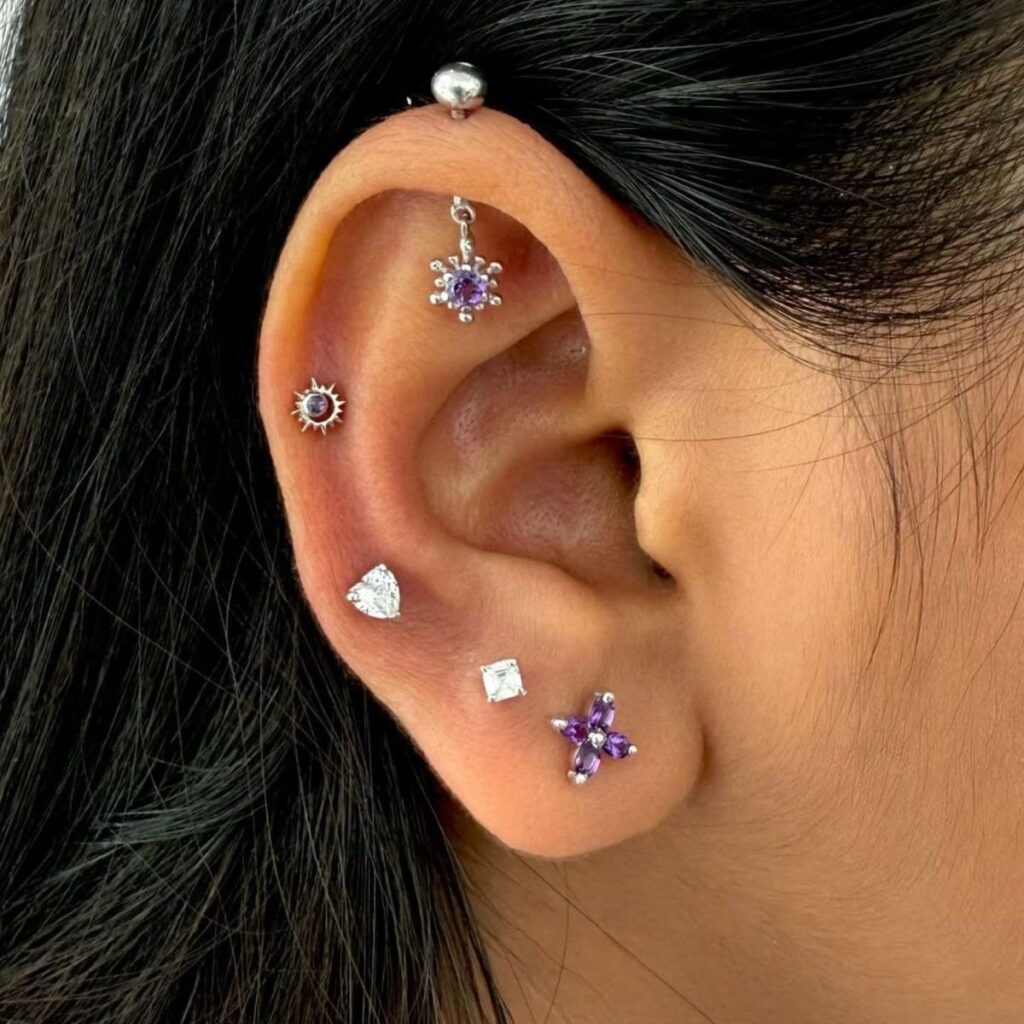 Ear with multiple piercings including a purple flower stud in the upper cartilage