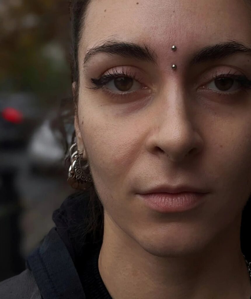 Person with a vertical bridge piercing featuring two silver studs between the eyebrows.