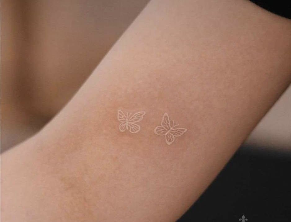 Two small white ink butterfly tattoos on a person's forearm.